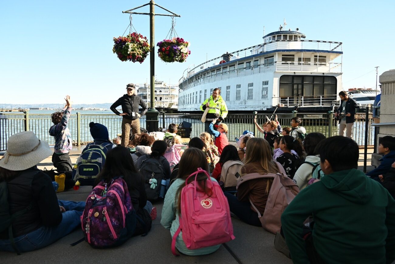 Image shows Exploratorium teacher Lori Lambertson leading an interactive king tides discussion with SFUSD students along the Embarcadero.